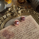 An angled view of the pink pearl earrings, highlighting the scalloped design and the soft, weathered patina of the antiqued bronze setting.