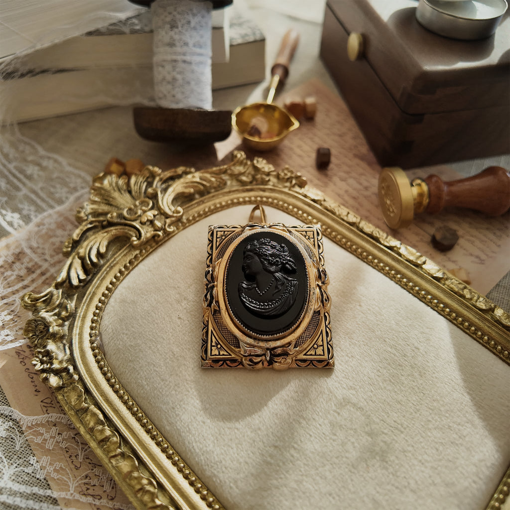 The "Hearthside," a 1940s antique Coro cameo brooch, featuring a carved black glass lady in profile set in a heavily worn, ornate gold-tone frame.