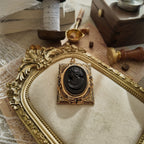 The "Hearthside," a 1940s antique Coro cameo brooch, featuring a carved black glass lady in profile set in a heavily worn, ornate gold-tone frame.