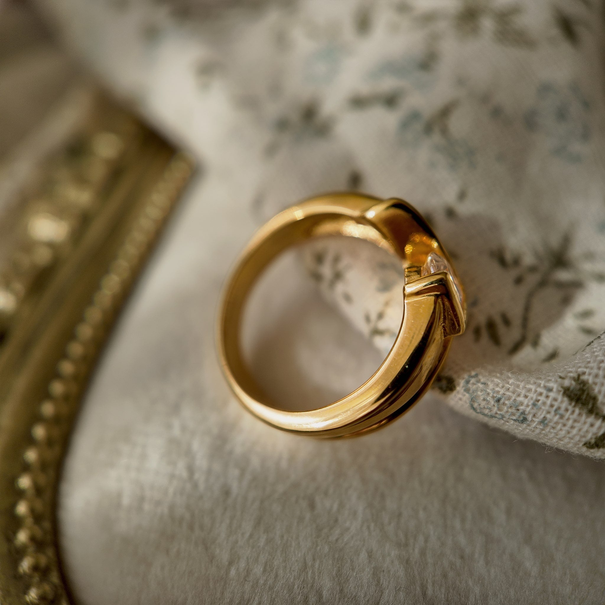 This 23k gold-plated ring features a square band set with round glass diamonds, while the band itself is made of plain gold with a simple geometric design. The complete band is shown from the side.