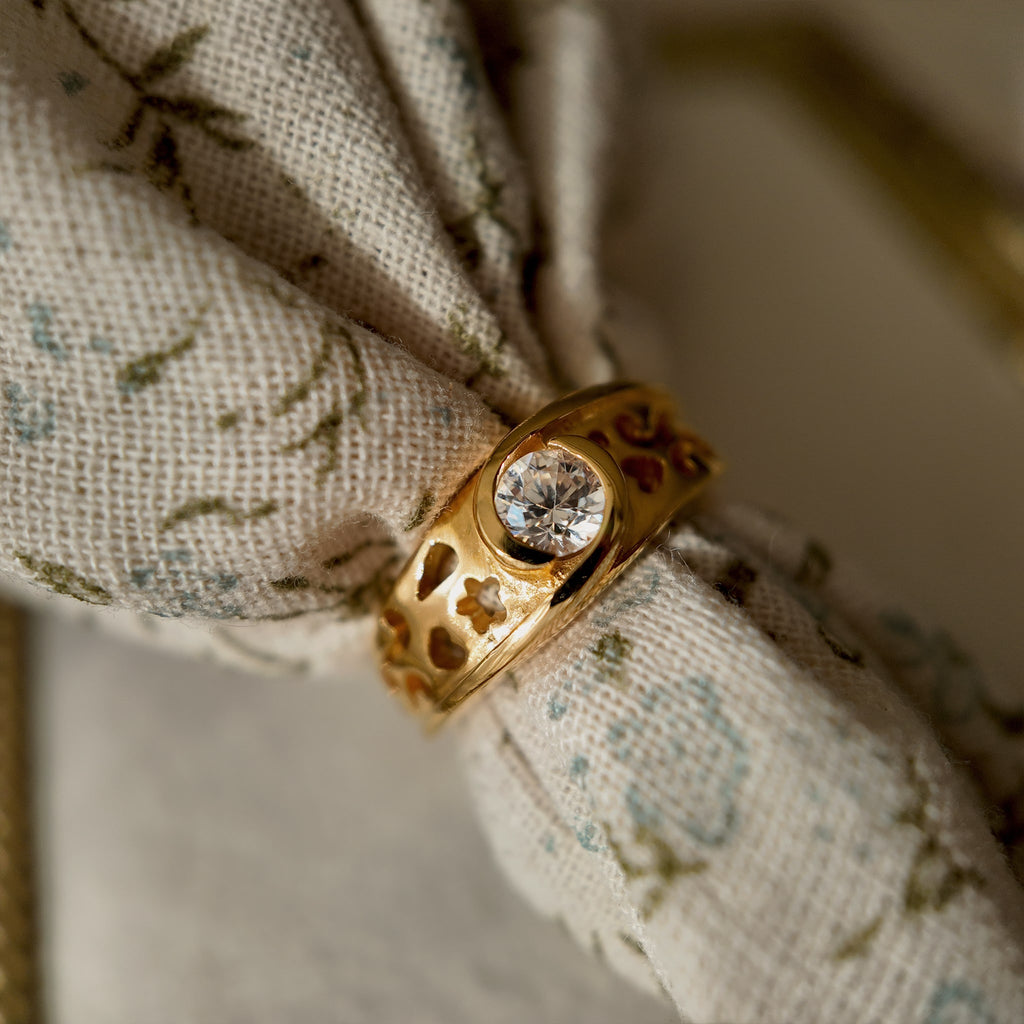 This 23k gold-plated ring features a round glass diamond set in a single piece, with the band openwork engraved with delicate patterns. It's a vintage ring with a retro style, featuring a gold band, 23k gold plating, and a glass diamond.