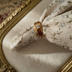 The 23k gold-plated ring features a round brilliant-cut glass diamond, and the band is openwork-carved with delicate patterns. The vintage ring is strung with floral fabric to simulate how it would look on a hand. The diamond is lustrous, and the band features cute patterns resembling auspicious clouds and hearts.