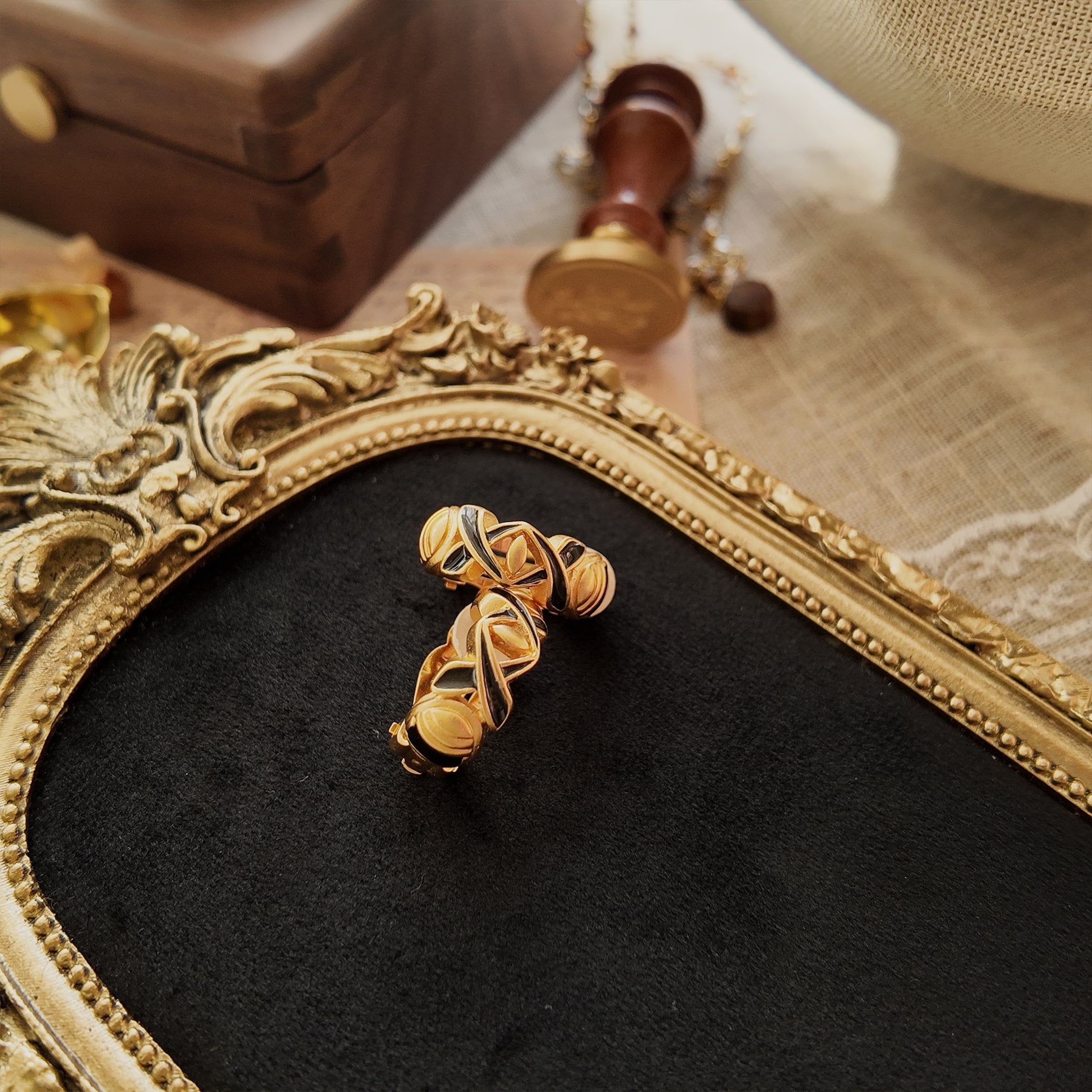 The matte gold-plated hoop ear clips are engraved with geometric patterns and paired with black enamel.