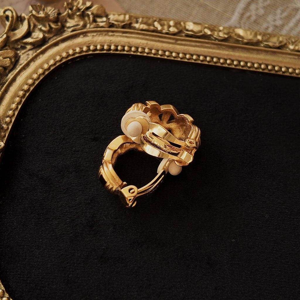 The display showcases stacked matte gold clip-on earrings, highlighting the craftsmanship on the back and the brand's embossed "D'Orlan" logo.