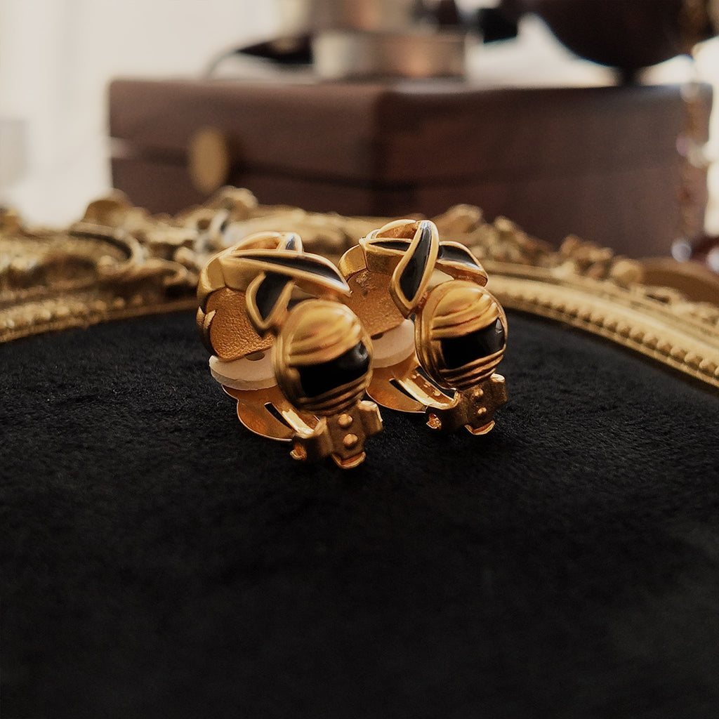 The gold clip-on earrings, viewed from below, showcase the engraved design and details of the black enamel on the lower part.