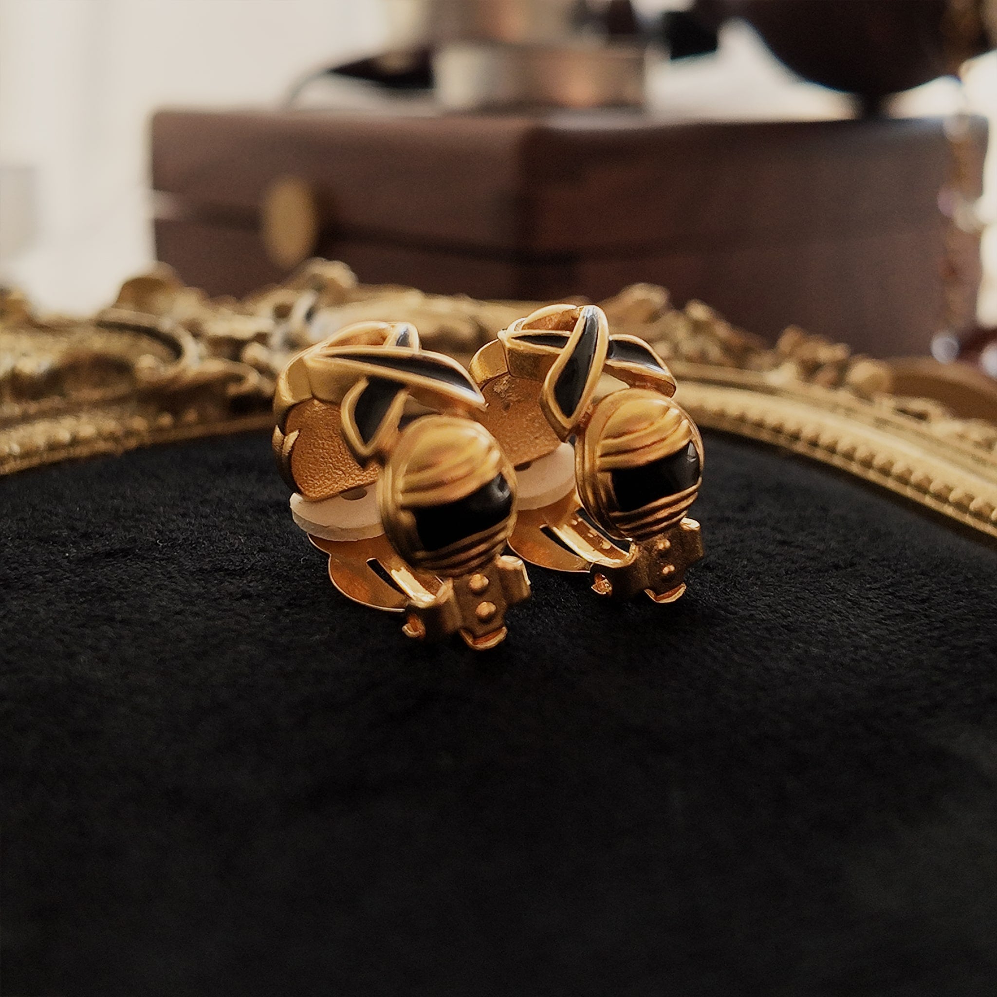 The gold clip-on earrings, viewed from below, showcase the engraved design and details of the black enamel on the lower part.