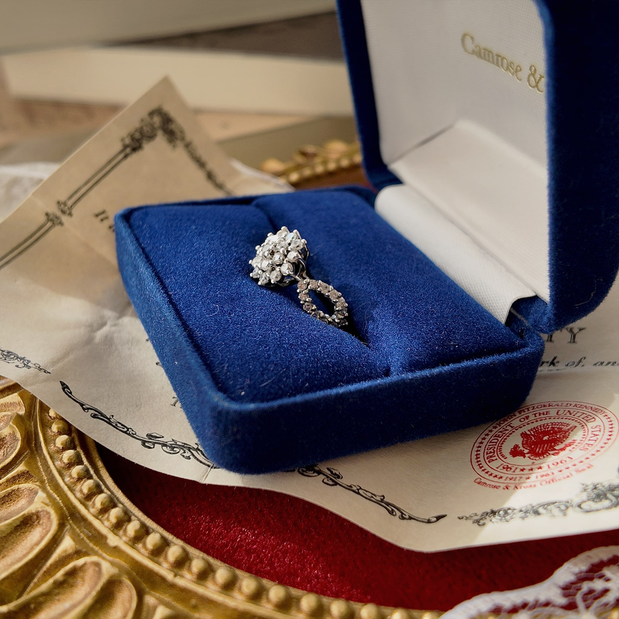 The ring is displayed up close inside its original box, featuring two openwork rings on the side set with several small rhinestones.