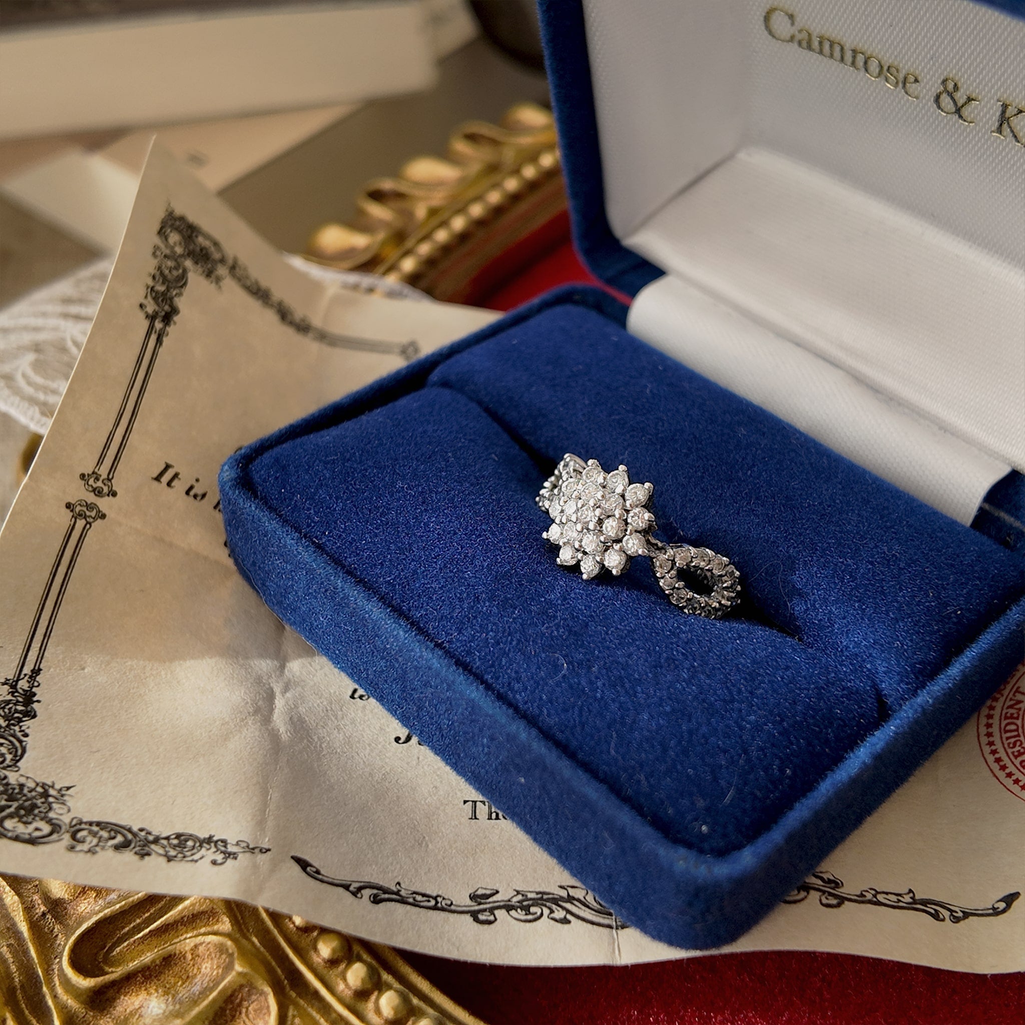 A close-up view of the ring inside its original box, showing the connection between the rhinestone design on the side and the central floral rhinestone cluster.