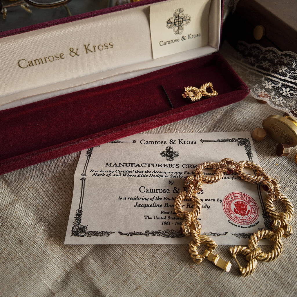 Camrose & Kross's gold-brushed bracelet, a collaboration with US First Lady JBK, features a red gemstone and comes with its original packaging and official brand certificate of authenticity.