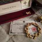 Camrose & Kross's gold-brushed bracelet, a collaboration with US First Lady JBK, features a red gemstone and comes with its original packaging and official brand certificate of authenticity.