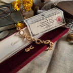 The gold-brushed bracelet, inlaid with red gemstones, sits on its original, open red velvet packaging box, alongside a complete official certificate of authenticity, showcasing its overall appearance.