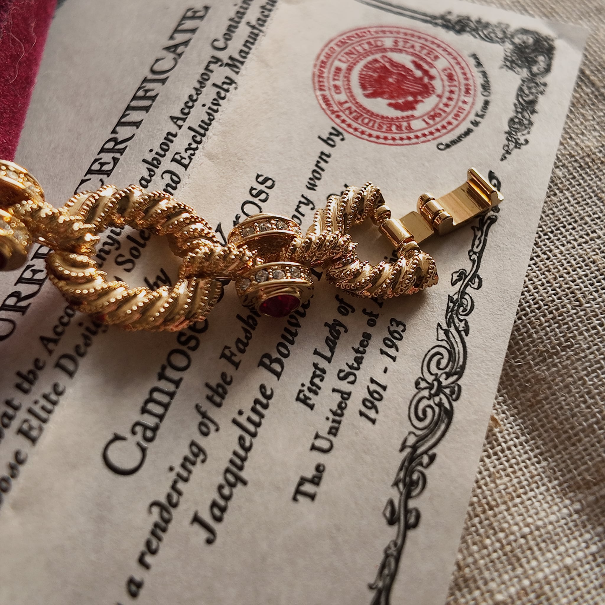 The gold bracelet's clasp details are showcased, with mini rhinestones set around the outer ring of the red gemstone at the bracelet's connection point, exuding luxury.