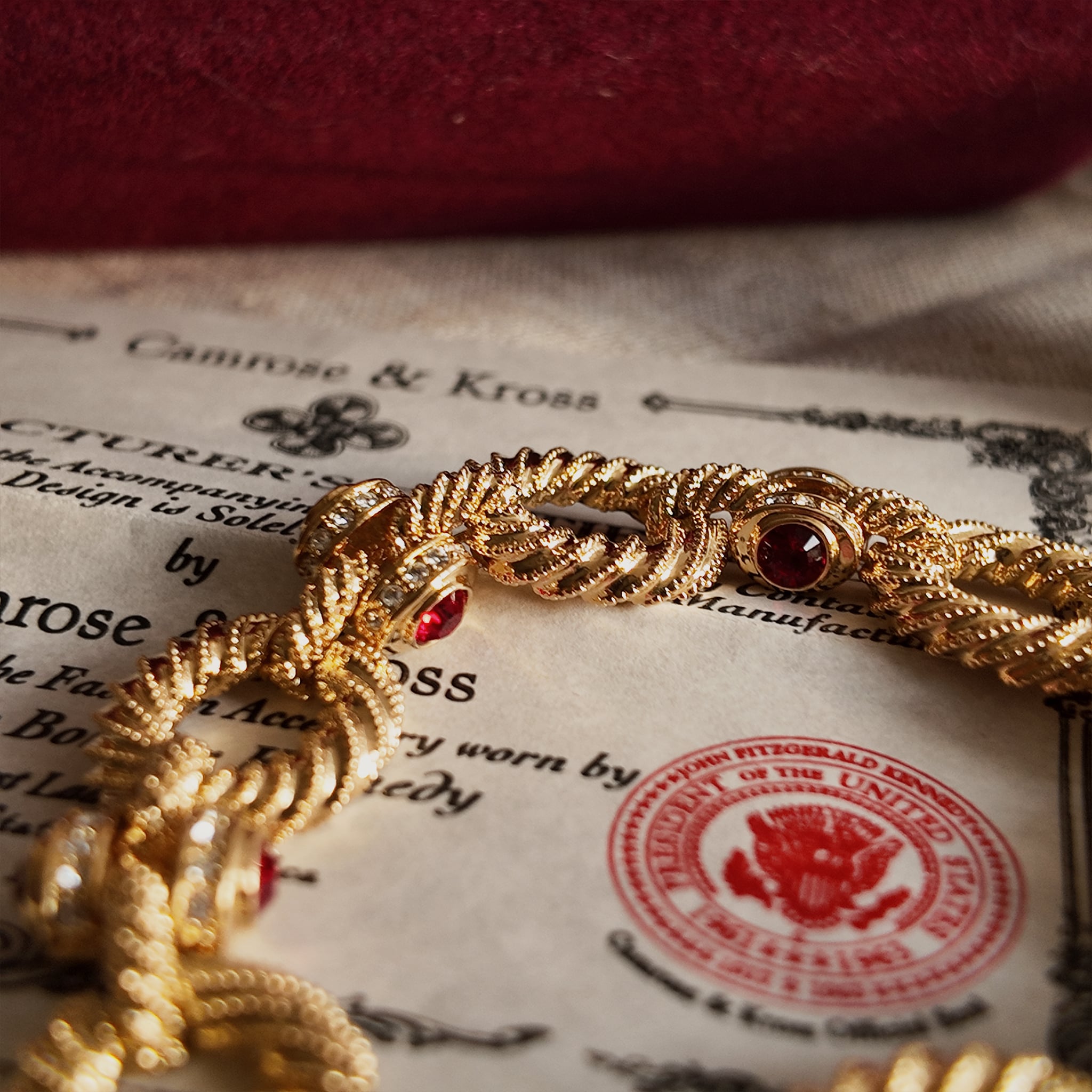 The gold-plated bracelet with red gemstones is placed on the official certificate of authenticity, with a magnified view of the details showing where the red gemstones connect to the bracelet.