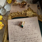 A colorful hummingbird brooch with a small green gemstone for its eye, which gleams with a rich golden hue in the sunlight.