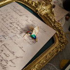 This colorful hummingbird brooch prominently features its wings, especially adorned with small rhinestones, showcasing its creative design. The enamel colors are vibrant and contain a pearlescent sheen.