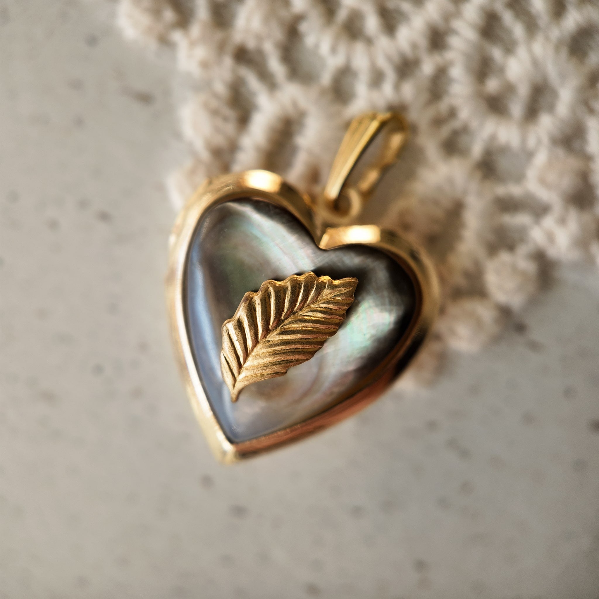 A heart-shaped photo box pendant with a small leaf on its black mother-of-pearl surface. Vintage sweetheart photo box pendant.