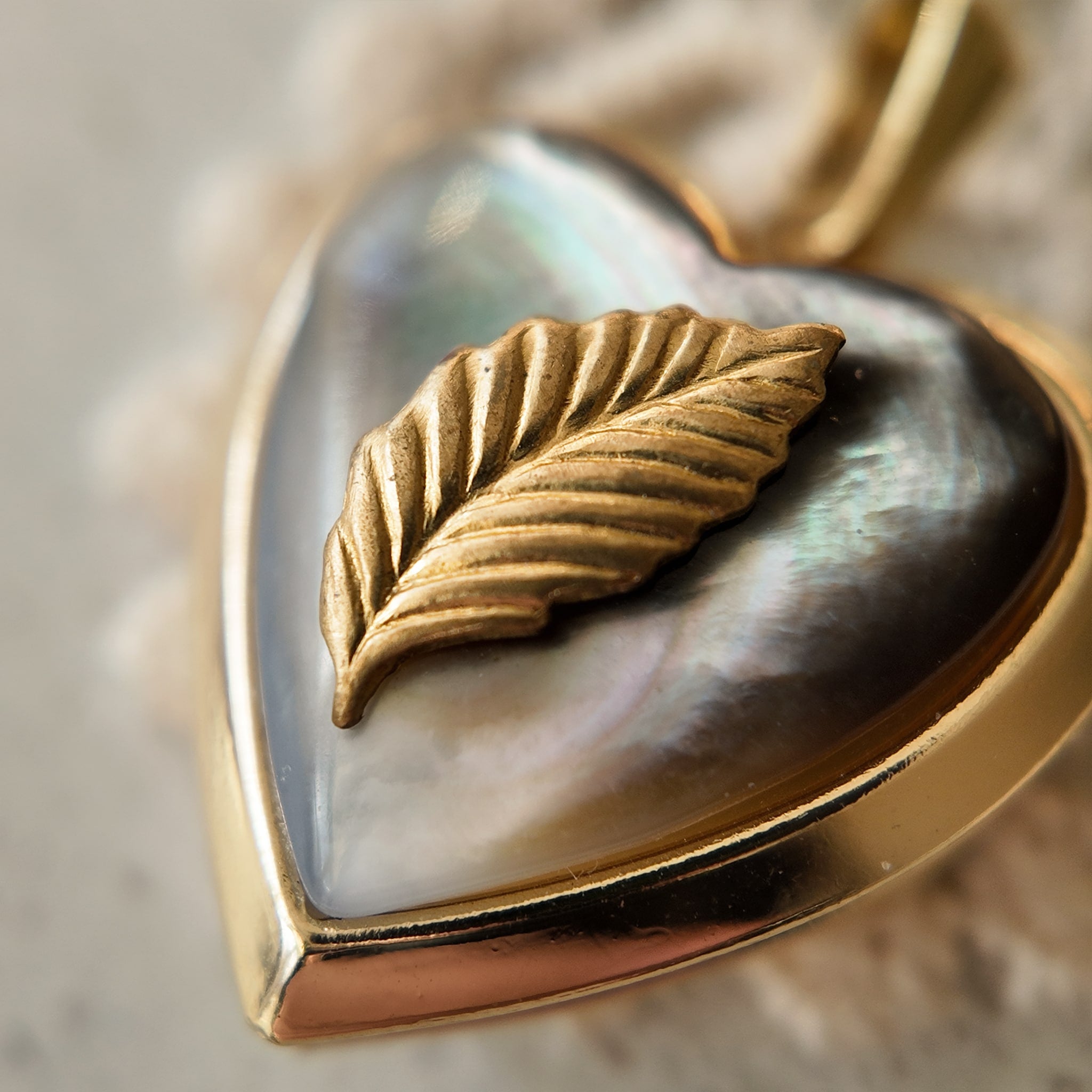A gold heart pendant with a black mother-of-pearl surface, featuring mother-of-pearl cloud patterns that shimmer like the aurora borealis. Mother-of-pearl jewelry, with its unique color, pearlescent sheen, and iridescent effect.