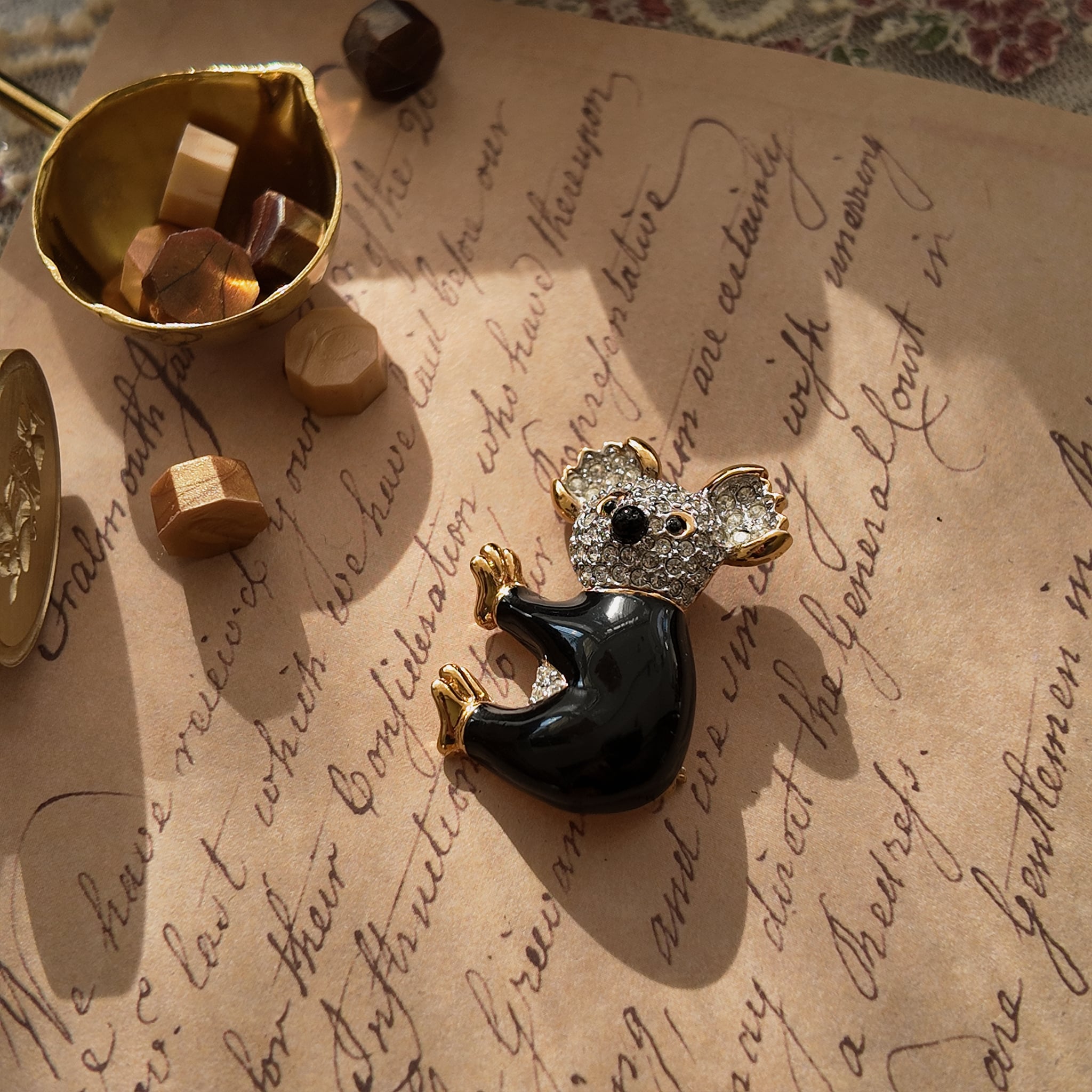 This koala brooch from D'orlan lies in the sunlight, showcasing the koala's back. The black enamel is rich and lustrous, and the gold-plated edging is exquisitely crafted.