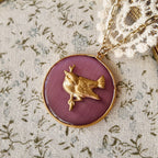 This round, rose-pink cat's-eye stone features a gold bezel and a cute little bird. The pink stone displays different colors and patterns under varying light. The bronze bird accessory is vintage and realistic. The pink-gold color is very retro and sweet; it's an American vintage pendant that looks incredibly charming paired with a gold necklace.
