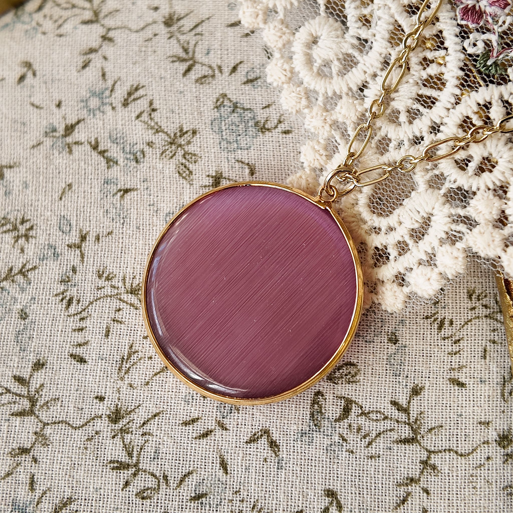 Pink cat's eye stone pendant necklace, featuring rose pink and magenta stone pendants. The stone is a pink, iridescent stone with a gold-plated rim and a lustrous finish.