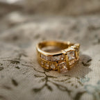 A gold ring set with two rows of glass diamonds is placed on a piece of floral fabric.