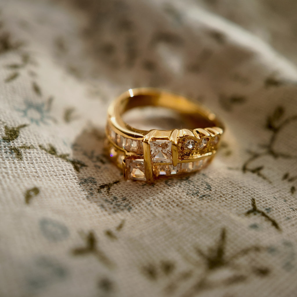 A gold ring set with two rows of glass diamonds is placed on a piece of floral fabric.