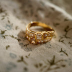 A gold ring set with two rows of glass diamonds is placed on a piece of floral fabric.