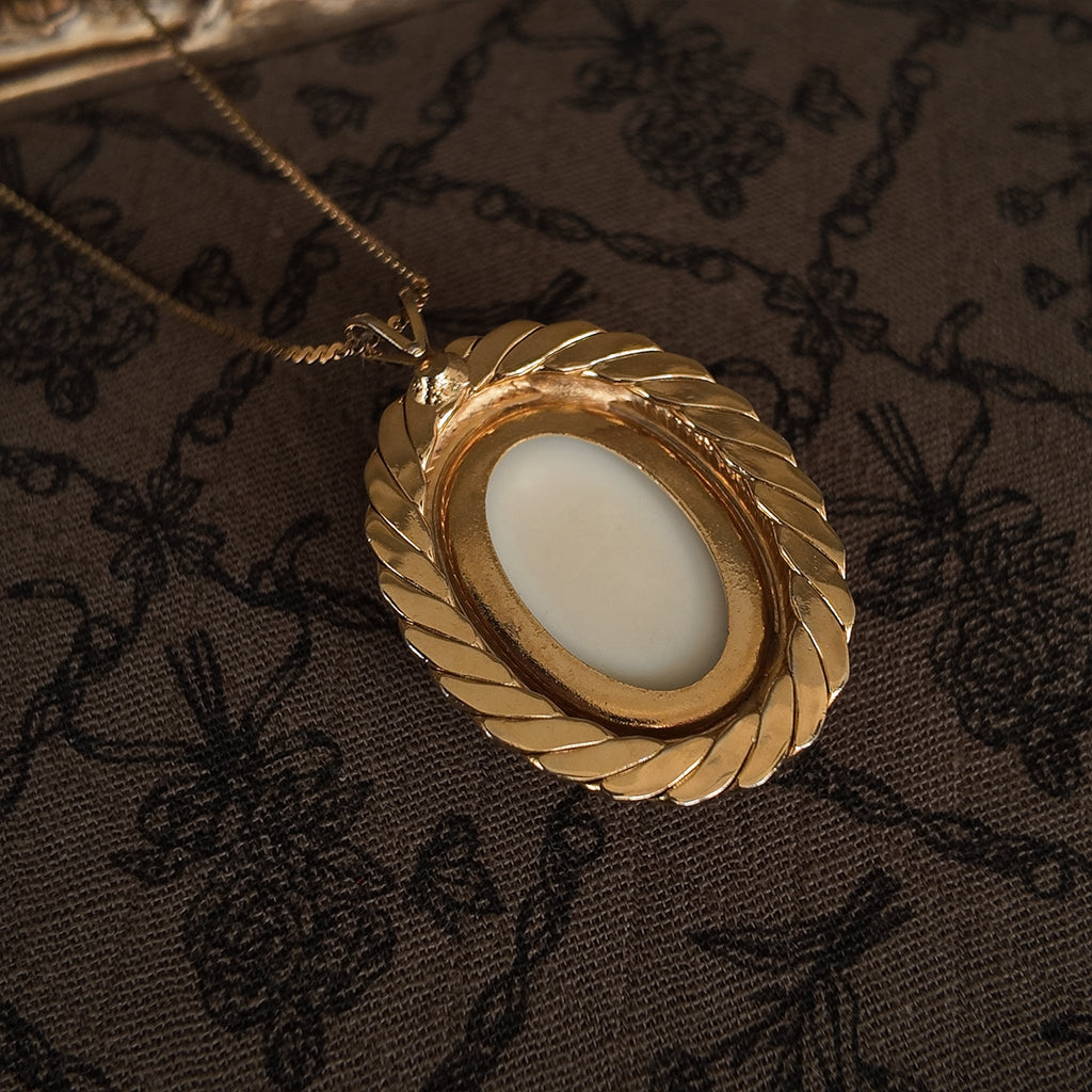 The back of the white stone-carved egg-shaped pendant is smooth and white with gold edging, and it is made of sterling silver.