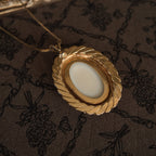 The back of the white stone-carved egg-shaped pendant is smooth and white with gold edging, and it is made of sterling silver.