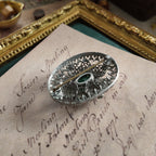 A close-up view of the back of a silver cloisonné brooch, showcasing the cloisonné design.