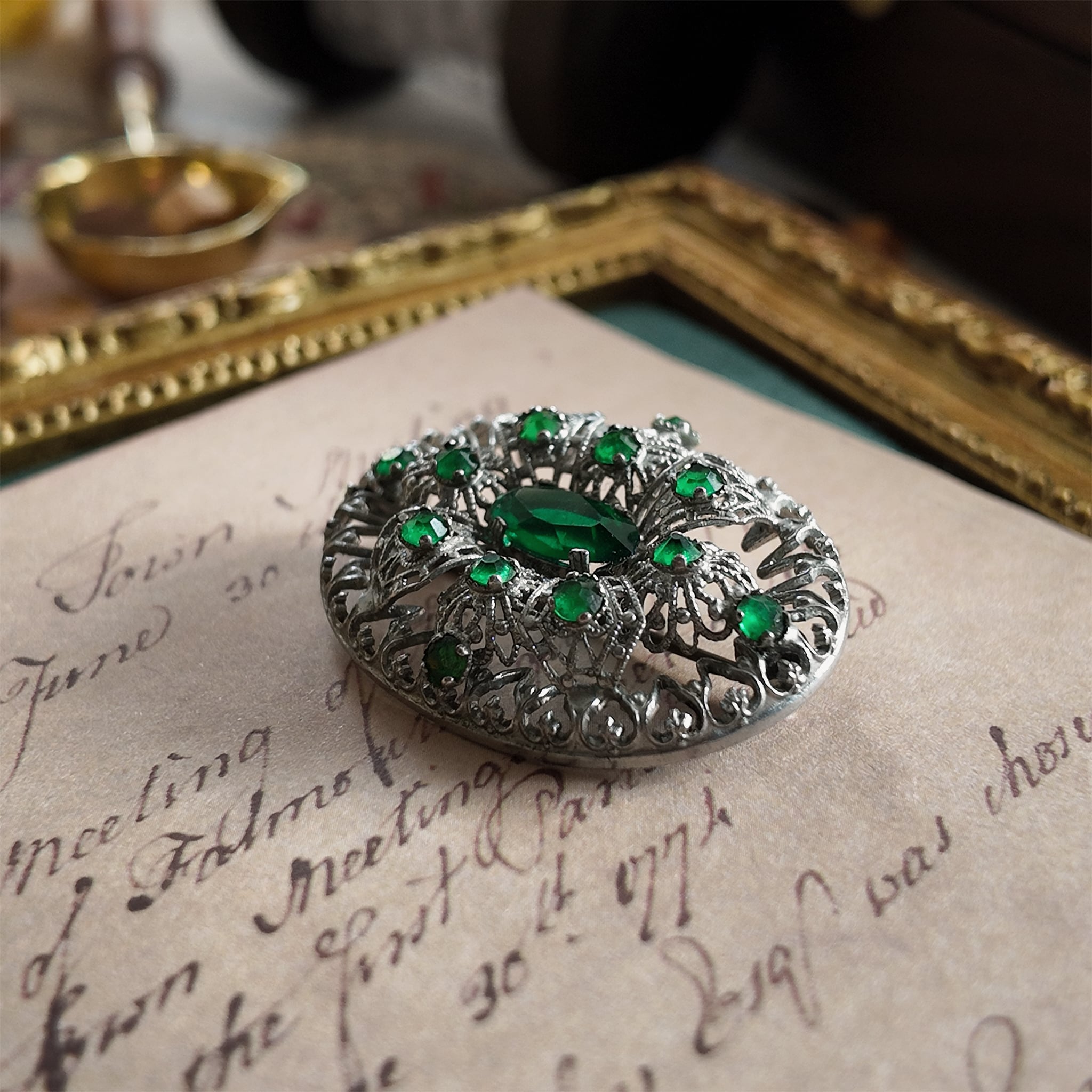 The silver cloisonné brooch is set with an emerald gemstone. A close-up side view highlights the texture of the central oval emerald gemstone.