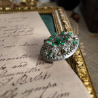 A silver cloisonné brooch set with emerald gemstones, showcasing the arched design on the brooch's surface from the side.