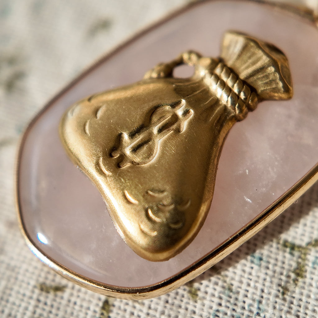 A cute money bag pendant with a cartoon money bag design on rose quartz crystal; a piece of money jewelry.