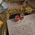 Vintage-style red gemstone with an aged gold frame; the red gemstone displays different colors under different lighting. A very elegant vintage piece of jewelry.