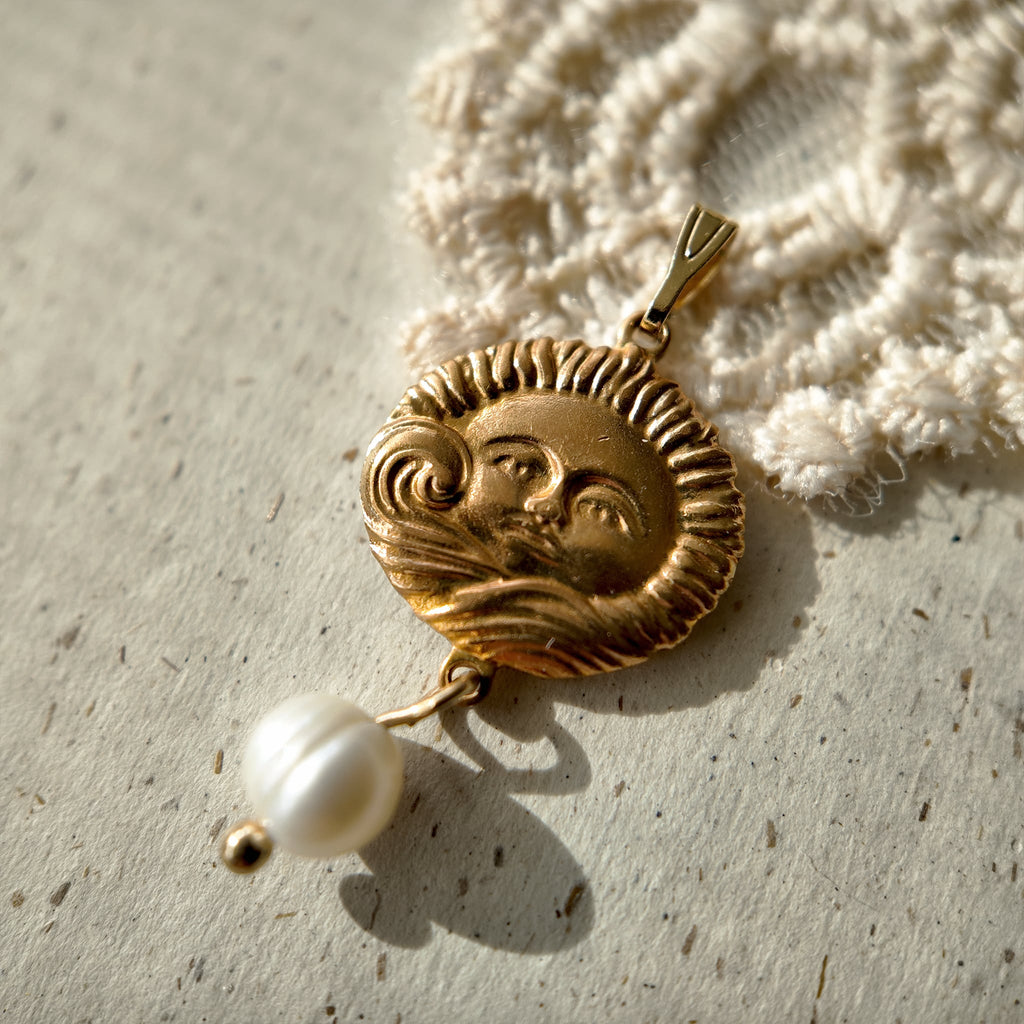 A golden brass pendant with freshwater pearls and an engraving of the sun god.