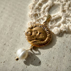 A golden brass pendant with freshwater pearls and an engraving of the sun god.