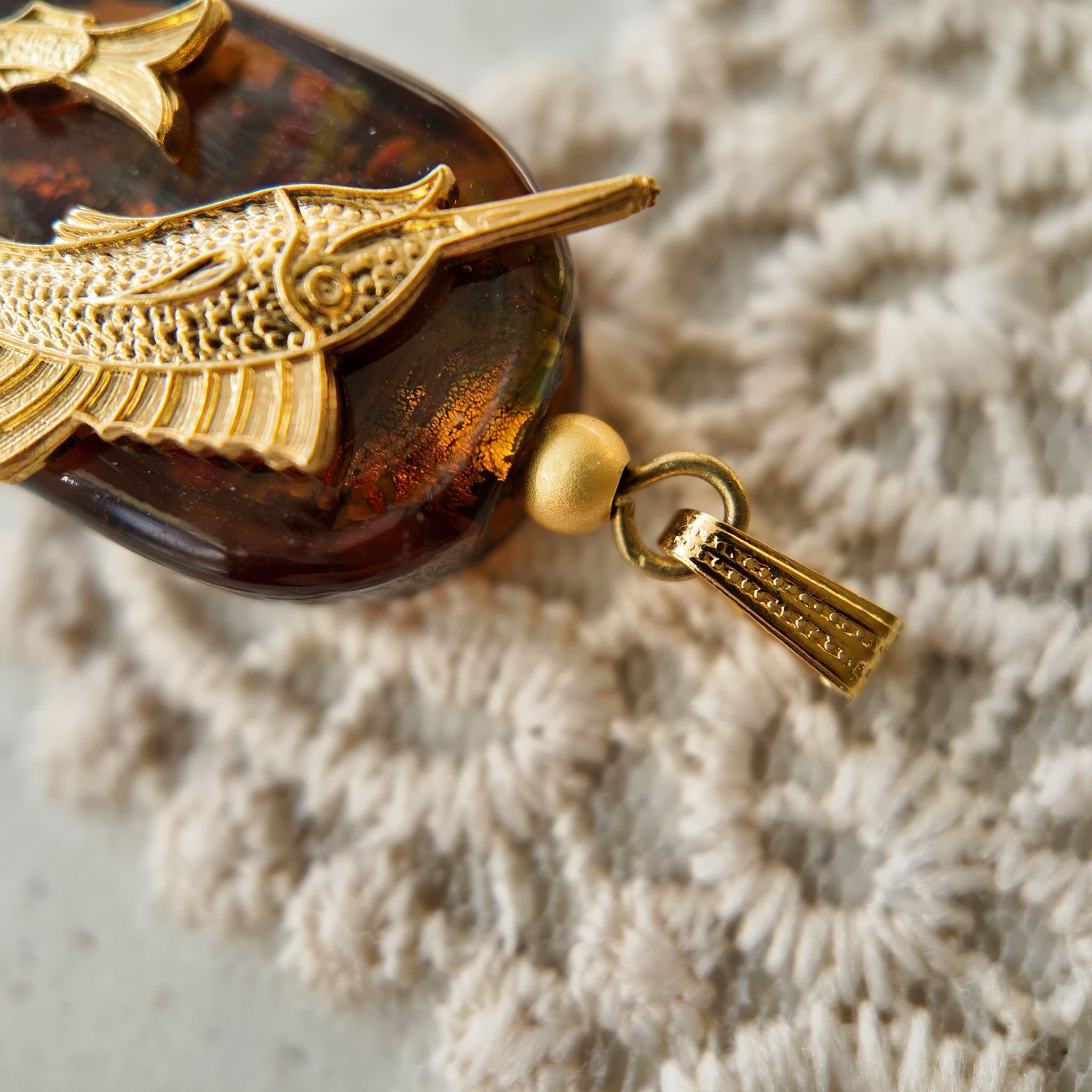 A macro shot detailing the unique, flower-like blue and green swirls suspended within the amber art glass, making each "Leaping Wanderer" charm one-of-a-kind.