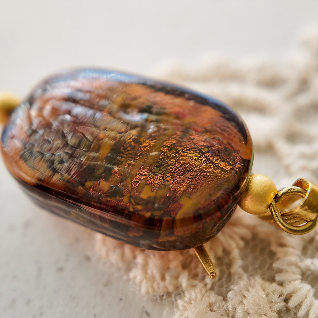 A macro shot detailing the unique, flower-like blue and green swirls suspended within the amber art glass, making each "Leaping Wanderer" charm one-of-a-kind.