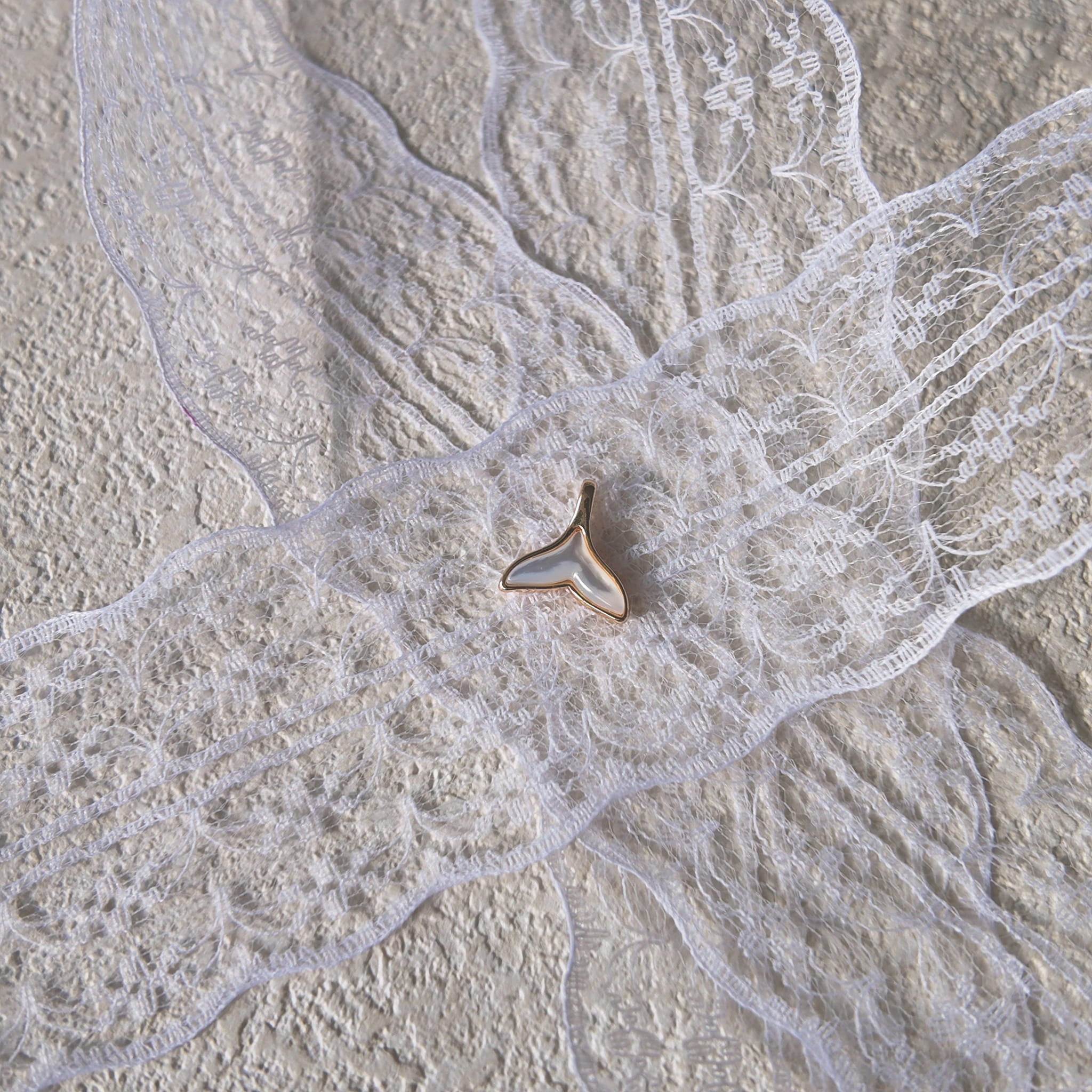 The minimalist mermaid tail charm styled on a piece of sea-worn driftwood to emphasize its "Oceanic Minimalism" and its identity as an amulet of freedom.