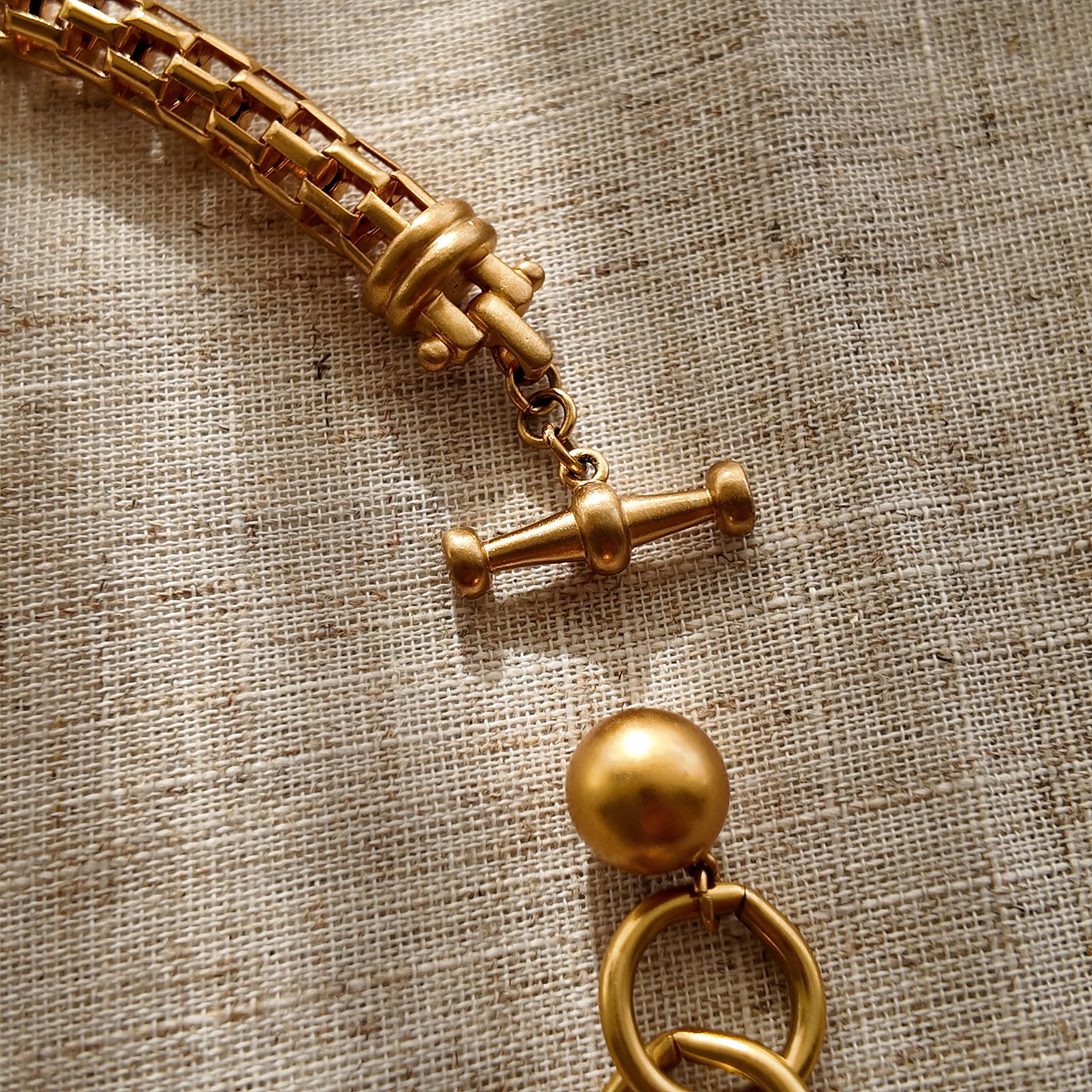 A macro shot detailing the unique, architectural plait design of the necklace chain and the organic, imperfectly perfect surface of a baroque pearl.