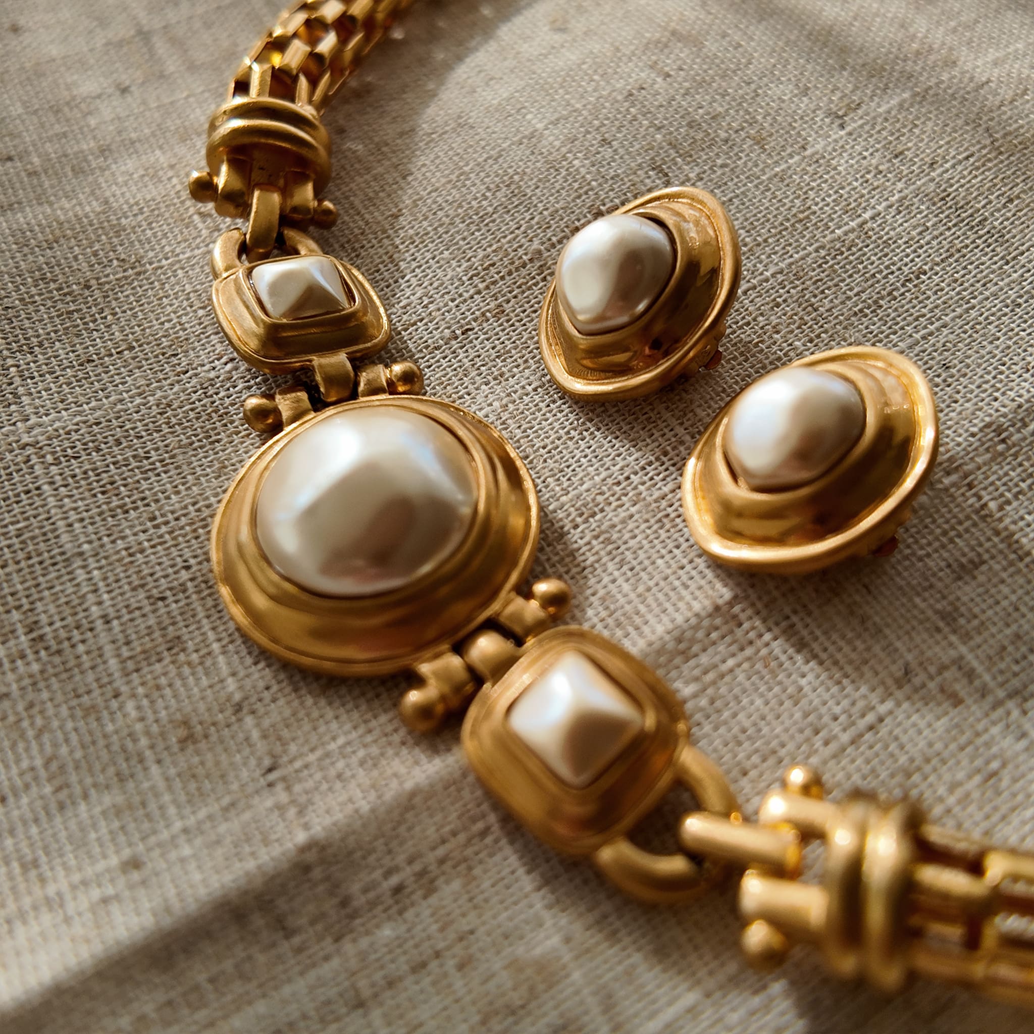 A pair of vintage Anne Klein clip-on earrings, featuring a central baroque pearl surrounded by a bold, circular frame with a rich, brushed matte gold finish.