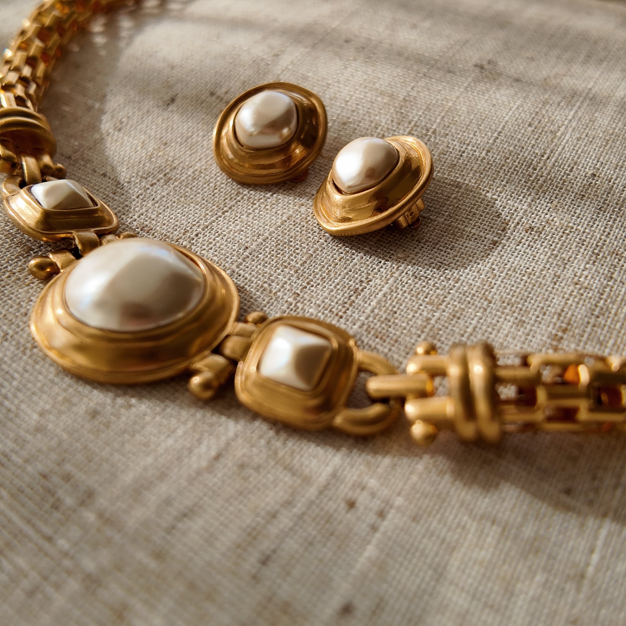 A pair of vintage Anne Klein clip-on earrings, featuring a central baroque pearl surrounded by a bold, circular frame with a rich, brushed matte gold finish.