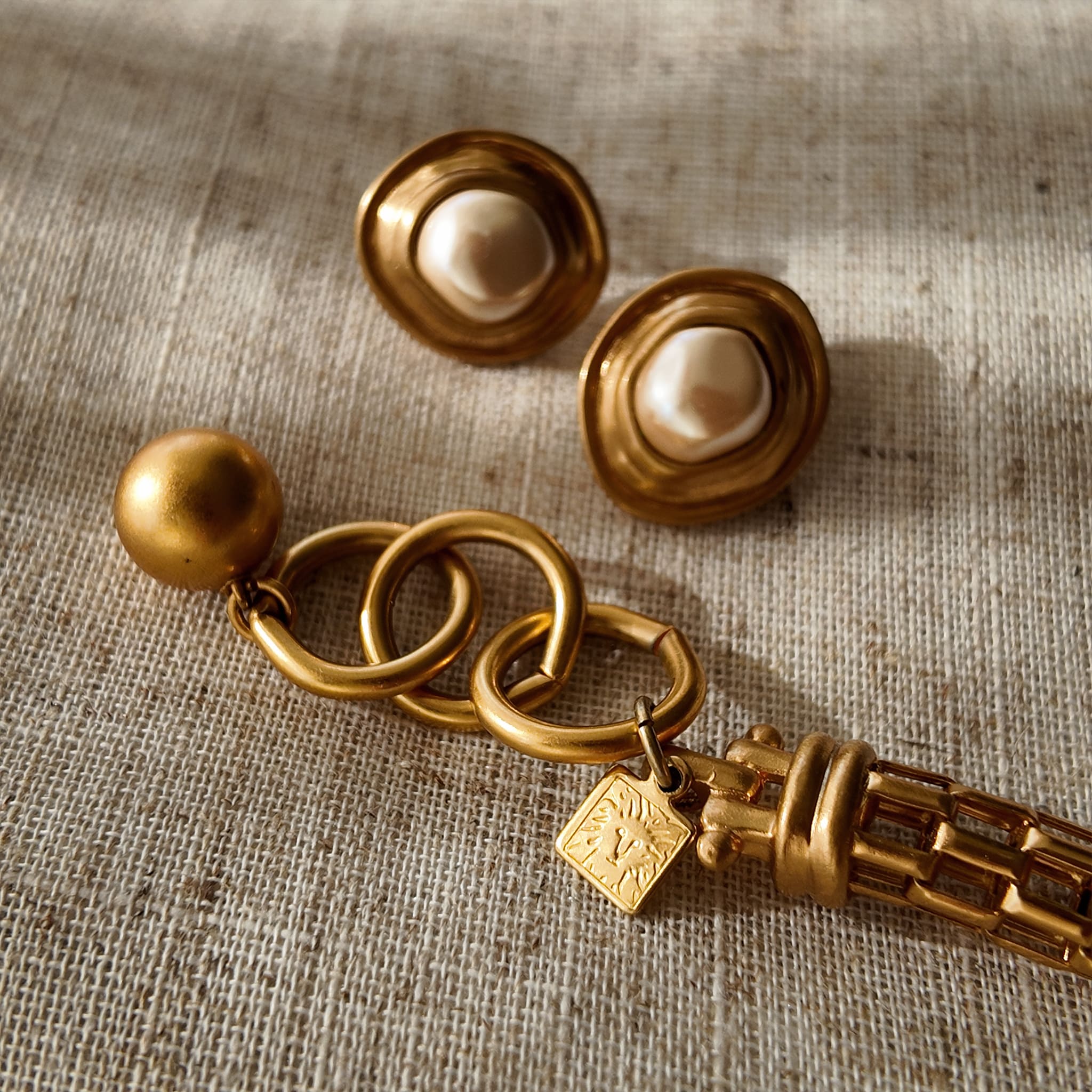 A detailed photo of the authentic Anne Klein signatures: the iconic lion head logo hang tag on the necklace and the signature "AK" hammered texture on the reverse.