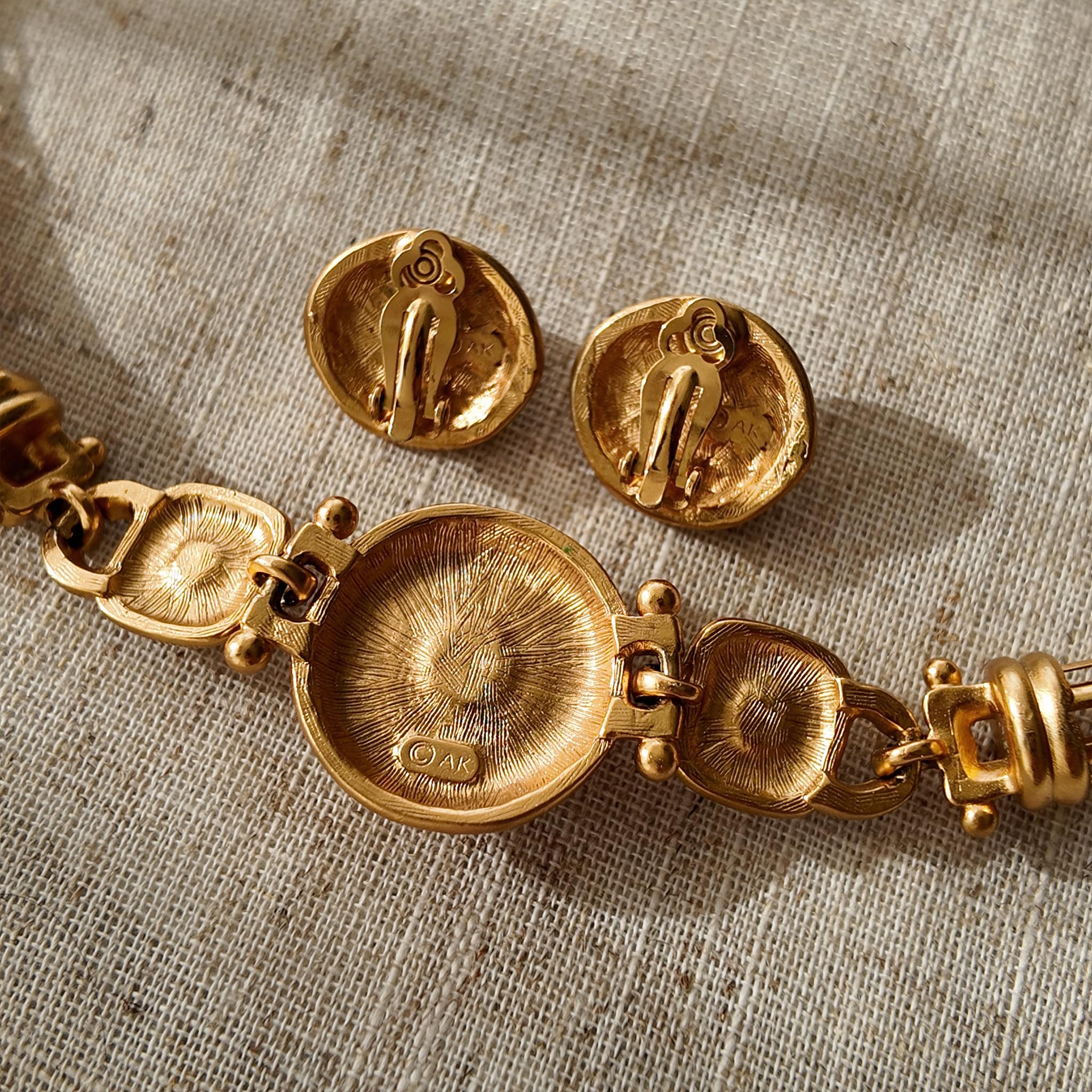 A detailed photo of the authentic Anne Klein signatures: the iconic lion head logo hang tag on the necklace and the signature "AK" hammered texture on the reverse.