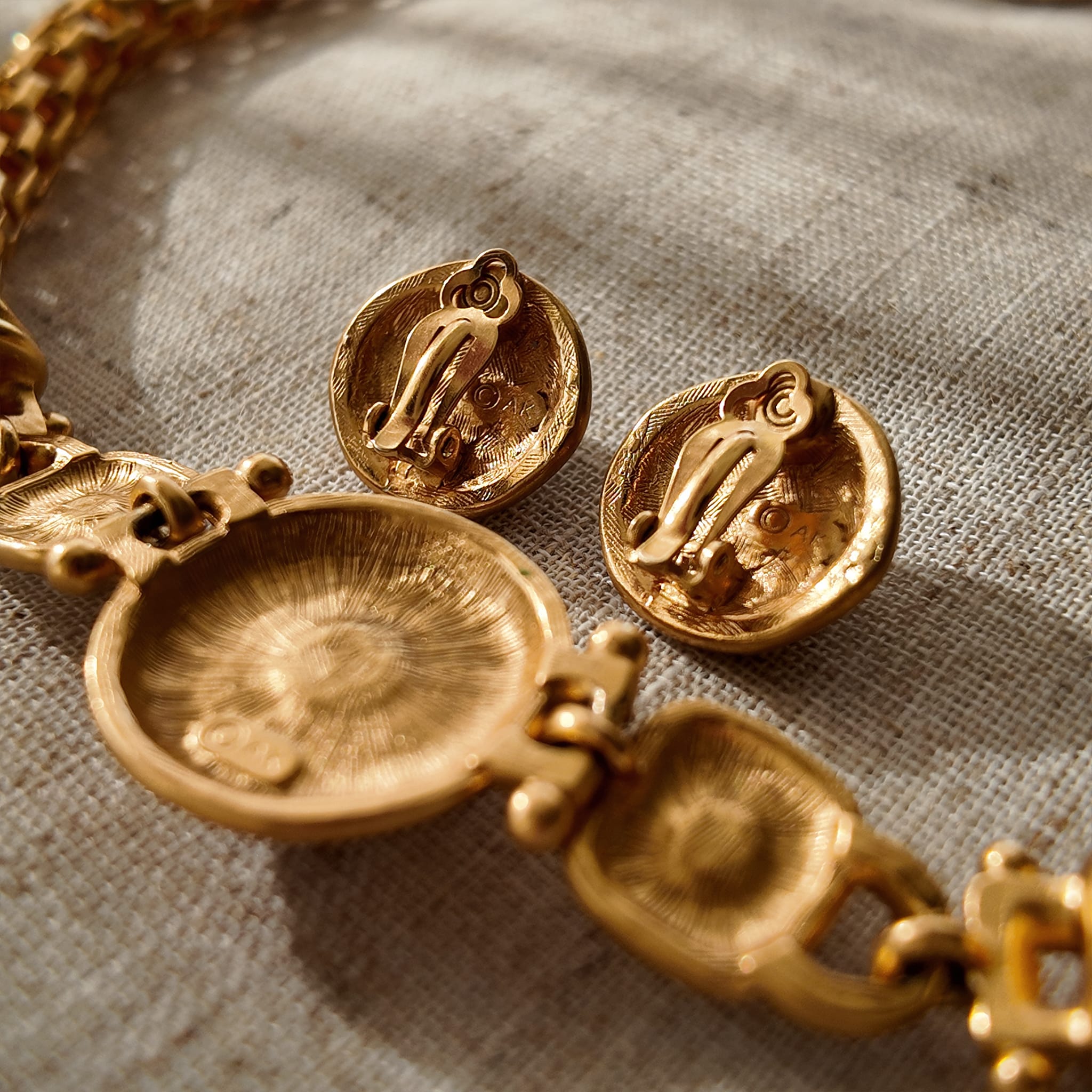 A detailed photo of the authentic Anne Klein signatures: the iconic lion head logo hang tag on the necklace and the signature "AK" hammered texture on the reverse.