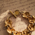 A detailed photo of the authentic Anne Klein signatures: the iconic lion head logo hang tag on the bracelet and the signature "AK" hammered texture on the reverse.