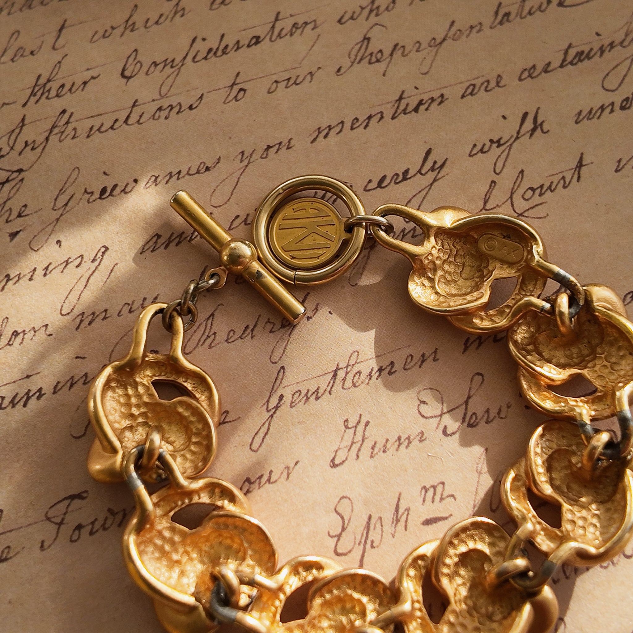 A detailed photo of the authentic Anne Klein signatures: the iconic lion head logo hang tag on the bracelet and the signature "AK" hammered texture on the reverse.