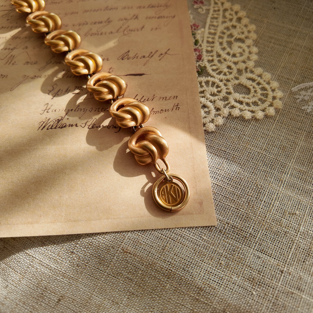 A detailed photo of the authentic Anne Klein signatures: the iconic lion head logo hang tag on the bracelet and the signature "AK" hammered texture on the reverse.