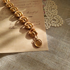 A detailed photo of the authentic Anne Klein signatures: the iconic lion head logo hang tag on the bracelet and the signature "AK" hammered texture on the reverse.