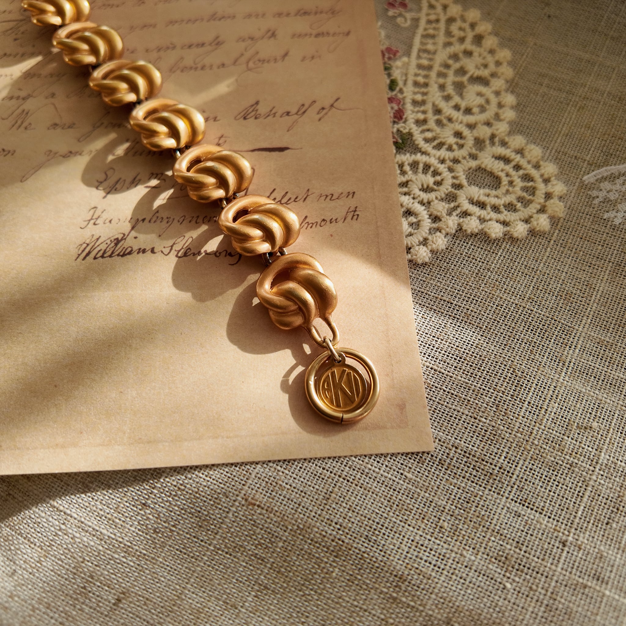 A detailed photo of the authentic Anne Klein signatures: the iconic lion head logo hang tag on the bracelet and the signature "AK" hammered texture on the reverse.